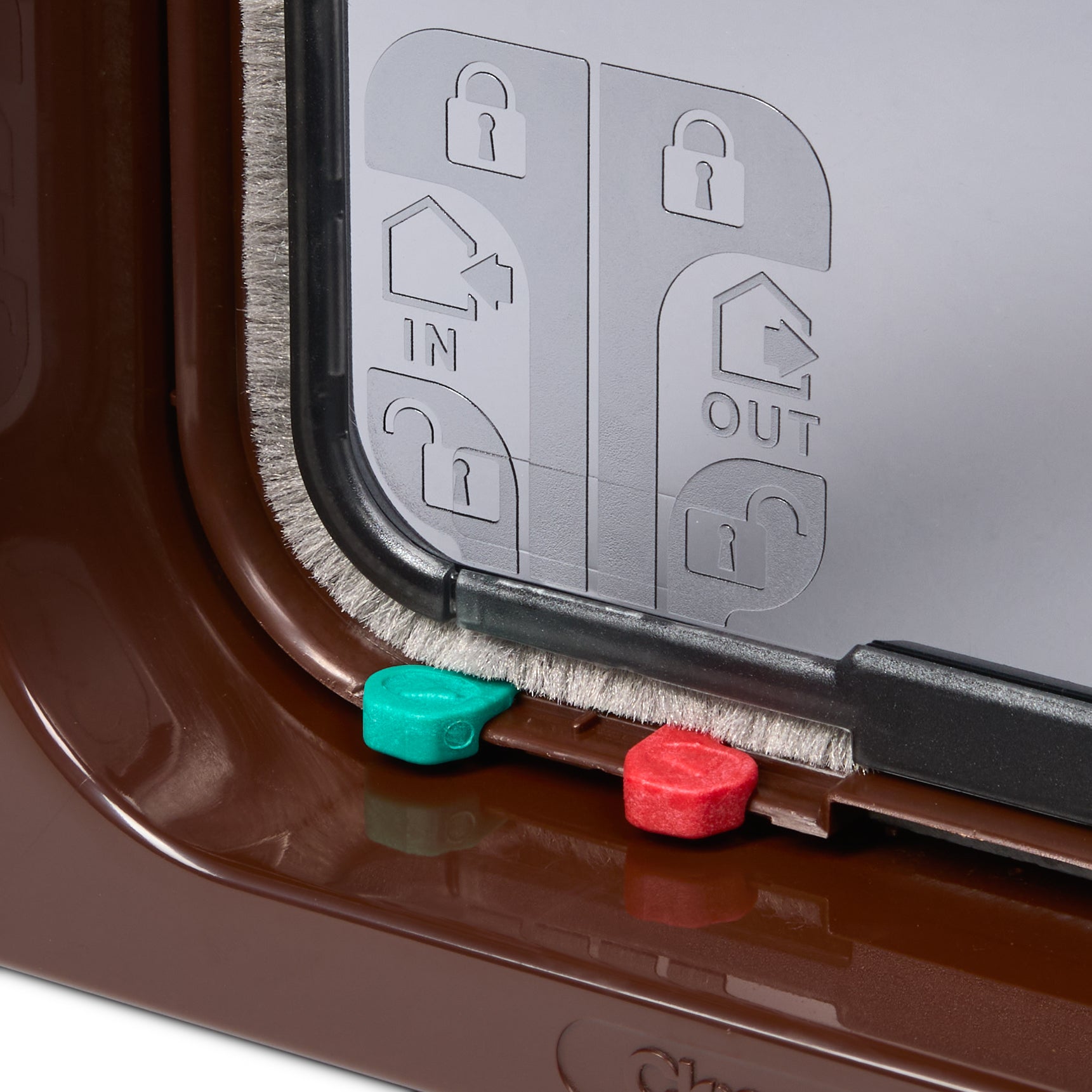 A close-up view of two of the red and green manual locks on the brown framed pet door for large cats and small dogs on a white background 