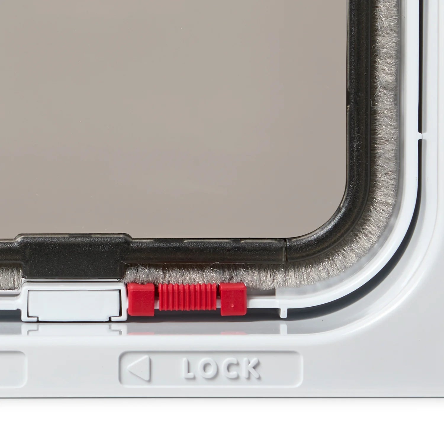 Close-up view of the red lock in the locked position on the white cat flap with the draught proof brush visible. 