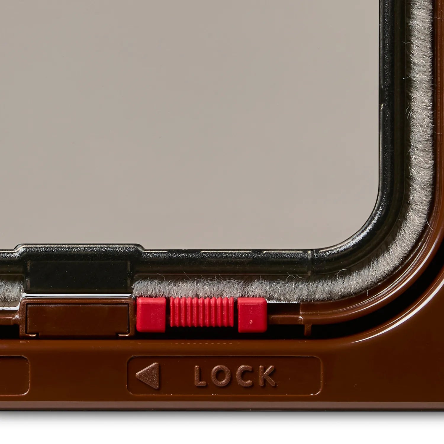 Close-up of a red lock mechanism on a brown pet door for cats. 